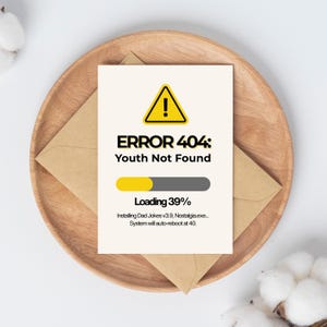 Peut inclure: Une carte de vœux humoristique avec le texte "ERROR 404: Youth Not Found" et une barre de chargement à 39%. La carte est sur une assiette en bois avec une enveloppe marron en dessous. La carte a un triangle jaune avec un point d'exclamation.