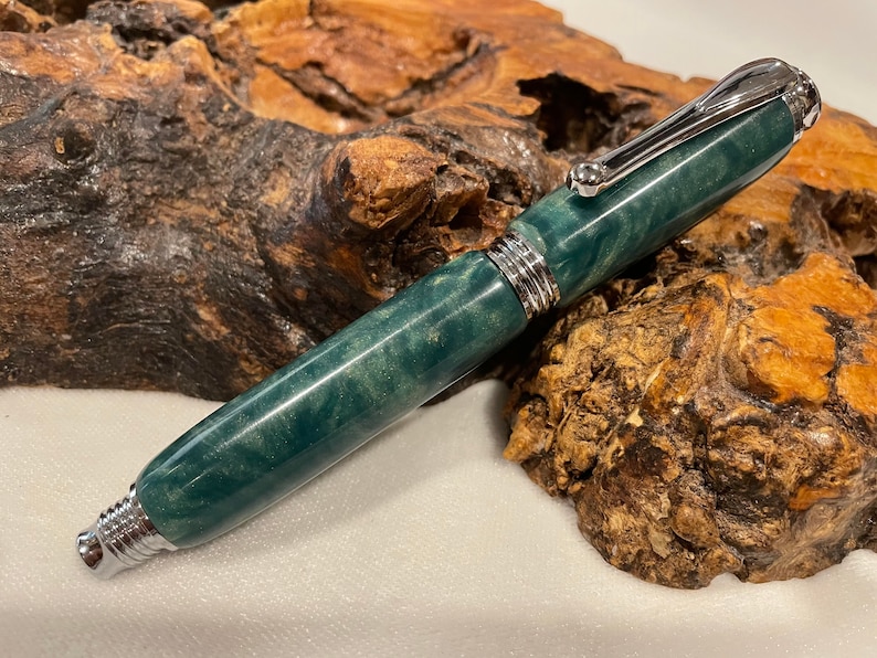 May include: A green and silver pen with a swirl pattern on the barrel. The pen is made of resin and has a silver clip and cap.