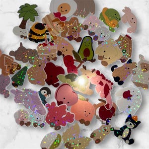 May include: A selection of colourful, glittery die-cut shapes with diverse designs. Includes a palm tree, bee, cupcake, star, avocado, bear, penguin, heart, and other cute characters. The shapes are in shades of brown, pink, green, and white.