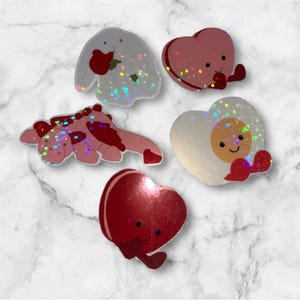 May include: A collection of five holographic stickers featuring a white rabbit holding a red flower, a pink heart-shaped character, a pink dragon-like creature, a heart-shaped fried egg character, and a solid red heart character with a face.
