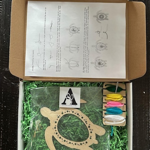 May include: A wooden turtle-shaped loom with numbered holes for stringing. The kit includes five spools of colorful embroidery floss and instructions for creating a string art design.