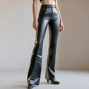 May include: Black, high-waisted, flared trousers with a crocodile skin texture. The trousers have a button closure and belt loops. The trousers are paired with black pointed-toe boots. The trousers are made of a shiny material.