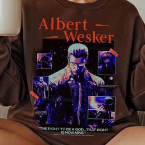 Puede incluir: Una sudadera marrón con un gráfico de Albert Wesker. El diseño incluye el texto "Albert - Wesker" en naranja, múltiples imágenes del personaje y la cita "THE RIGHT TO BE A GOD... THAT RIGHT IS NOW MINE."