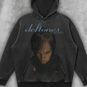 May include: Dark gray hoodie featuring the band name "Deftones" in light blue, with the album title "around the fur". The hoodie has a front pocket and a hood. The image on the front is a portrait of a person.