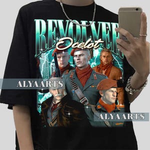 Könnte beinhalten: Schwarzes T-Shirt mit einem Grafikdesign mit dem Wort "REVOLVER" in Türkis, dem Namen "Ocelot" und Bildern von Charakteren. Das Shirt hat auch den Text "ALYAARTS" in Weiß.