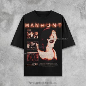 May include: Black t-shirt featuring the word "MANHUNT" in orange, with a pixelated image of a face and three smaller images. The shirt also includes text about the game and the Etsy shop's URL.