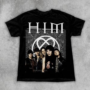 May include: Black t-shirt with a band photo and the band name "HIM" in white. The shirt features a heartagram symbol within a circular design. The band members are visible. The Etsy shop name is visible at the top of the image.