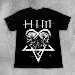 Puede incluir: Camiseta negra con un diseño gráfico blanco. El diseño incluye la palabra "HIM" sobre dos calaveras entrelazadas en forma de corazón, con un pentagrama debajo. El nombre de la tienda Etsy "Alyaartsdesign.etsy.com" es visible.