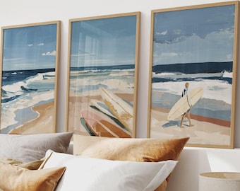 Puede incluir: Un conjunto de tres cuadros de pared que representan una escena de playa costera. Las obras muestran olas azules, orillas arenosas y tablas de surf. Una lámina muestra a una persona cargando una tabla de surf junto al agua.