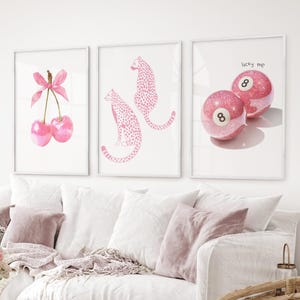 May include: Three framed art prints with pink designs. One shows two cherries with a pink bow. Another displays two pink cheetahs. The third print has two pink 8-ball pool balls with the text "lucky me".