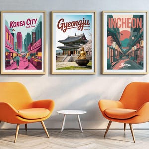 May include: Three framed travel posters with gold frames, each depicting a different South Korean city: Korea City, Gyeongju, and Incheon. The posters are displayed above two orange armchairs and a small white table.