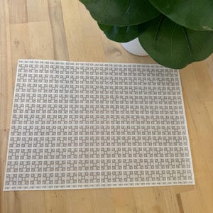 May include: A white placemat with a repeating pattern of grey squares and circles. The placemat is on a wooden surface.