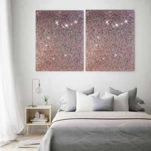 Puede incluir: Una cama gris con almohadas blancas y grises, una peque&ntilde;a mesita de noche de madera con una l&aacute;mpara y una planta, y dos grandes lienzos de purpurina rosa en la pared.