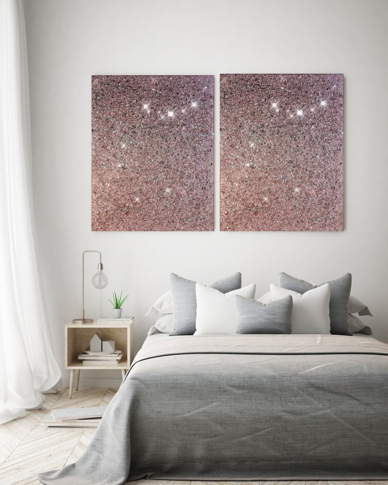 Puede incluir: Una cama gris con almohadas blancas y grises, una peque&ntilde;a mesita de noche de madera con una l&aacute;mpara y una planta, y dos grandes lienzos de purpurina rosa en la pared.