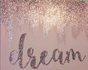 May include: A pink canvas with a glittery rose gold background and the word "dream" written in glitter.