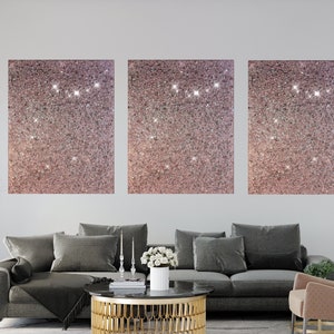 Puede incluir: Tres lienzos cuadrados con un fondo de purpurina rosa. Los lienzos est&aacute;n colgados en una pared blanca sobre un sof&aacute; gris.