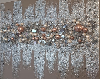 May include: A beige canvas painting with a silver glitter background. The glitter is arranged in vertical stripes. The painting is decorated with small, white pearls and rose gold beads.