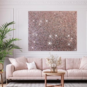 Puede incluir: Un sof&aacute; rosa con un coj&iacute;n blanco en una sala de estar con una gran obra de arte de pared de purpurina rosa, una planta en maceta y una mesa de caf&eacute; con un jarr&oacute;n de flores secas.