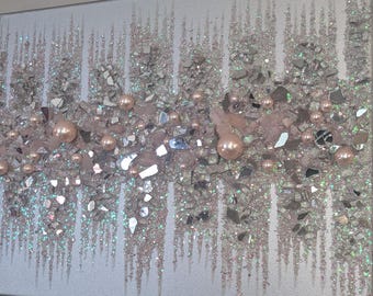 May include: A silver and pink abstract art piece with a glittery texture. The piece is made with broken glass, glitter, and pearls.