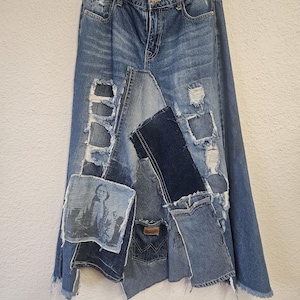 May include: A patchwork denim skirt with a distressed design. The skirt features various shades of blue denim, with ripped and patched sections. A small image is sewn onto the skirt. The skirt is hanging on a metal hanger.