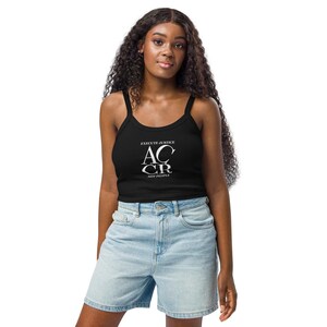 May include: Black tank top with the text "EXECUTE JUSTICE AC CR NOT PEOPLE" in white. The top has thin straps and is paired with light blue denim shorts. The model has long, curly black hair.