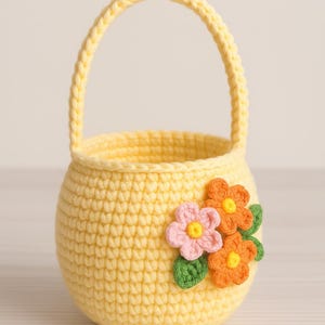 May include: A small yellow crocheted basket with a handle and three crocheted flowers in pink, orange, and green.