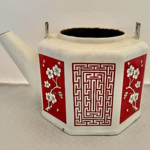 May include: White teapot with red and white floral designs and a red geometric pattern. The teapot has a rounded spout and a lid with a handle.