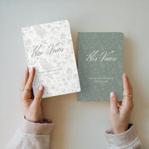May include: Two notebooks, one white with floral pattern and one sage green with floral pattern, are held up. The white notebook reads "Her Vows" and the green notebook reads "His Vows". Both notebooks have the names "DANIEL AND JENNIFER" and a date.