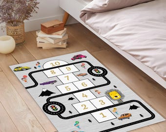 May include: A rectangular grey rug with a hopscotch grid and a road design. The rug features numbers 1-10, cars, traffic lights, and cartoon characters. The rug is designed for children's play and is placed on a wooden floor.