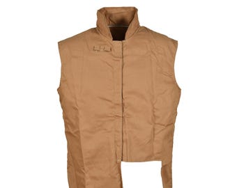 May include: A sleeveless tan vest featuring a high stand-up collar and a front placket with a small buckle detail near the neckline. The garment has an asymmetrical hemline with a longer panel on the left side and a shorter cut on the right.