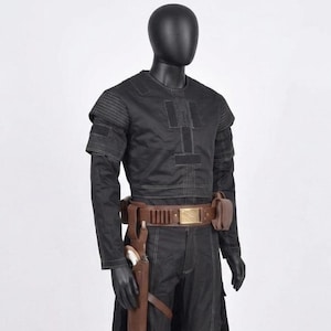 May include: Black costume with a brown belt and holster. The costume features a long-sleeved top with vertical stitching and matching trousers. The belt has a gold-coloured buckle and a brown holster with a white object.