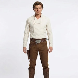 May include: A long-sleeved cream-colored shirt with a high collar, paired with brown trousers featuring a yellow side stripe. A brown leather belt with a metallic buckle and a holster is worn at the waist, complemented by tall brown leather boots.