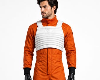 May include: A bright orange jumpsuit featuring a high collar, long sleeves with black ribbed cuffs, and multiple cargo pockets on the legs. A white, horizontally ribbed chest vest is worn over the jumpsuit, paired with black gloves and boots.
