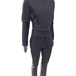 May include: A two-piece outfit in dark gray, featuring a cropped top and matching pants. The top has a high collar, long sleeves, and white stitching details. The pants have a button closure and patches on the knees. The outfit is displayed on a mannequin.