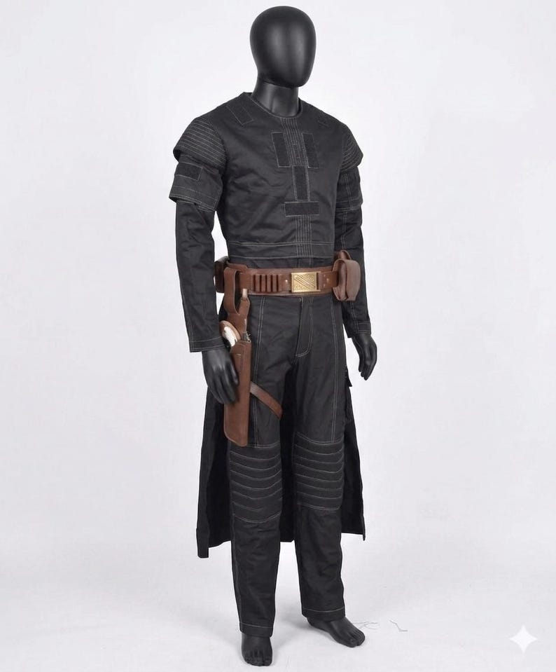 Op de afbeelding: Een zwart kostuum tentoongesteld op een mannequin. De outfit bevat een top met lange mouwen, een broek en een riem met zakjes. Een holster met een pistool is aan het been bevestigd. Het kostuum heeft een futuristisch ontwerp met zichtbare stiksels en gewatteerde details.