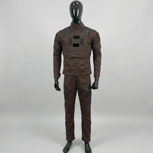 Op de afbeelding: Een bruin tactisch uniform gepresenteerd op een mannequin. De outfit bevat een jas met lange mouwen met versterkte schouder- en borstpanelen, en een bijpassende broek met zakken. De mannequin heeft een zwarte kop en handen.