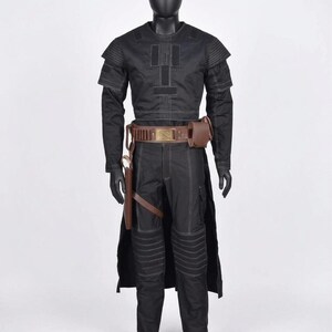 Op de afbeelding: Een zwart kostuum op een mannequin. De outfit bevat een top met lange mouwen met witte stiksels, een bijpassende broek, een bruine riem met een tasje en een holster. Het kostuum heeft een futuristische of militaire uitstraling.