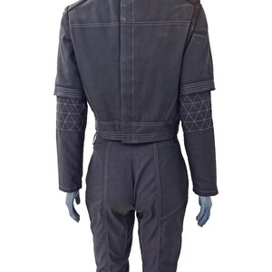May include: Dark gray jumpsuit with white stitching and geometric patterned accents on the sleeves. The jacket has a cropped waist and a brown collar. The pants are fitted with visible seams.
