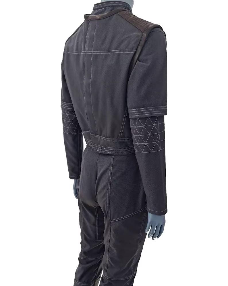 May include: A dark gray jumpsuit with white stitching details. The jumpsuit features a stand-up collar, shoulder pads, and geometric patterns on the sleeves. The back view shows the tailored fit and design of the one-piece garment.