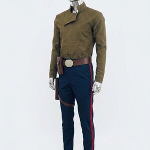 May include: A long-sleeved olive green shirt with a high collar and an asymmetrical front closure. The outfit includes dark blue trousers featuring a vertical red stripe down each leg, paired with a brown leather belt and an attached holster pouch.