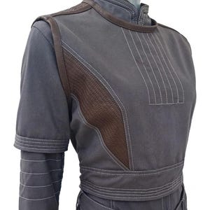 May include: A gray jumpsuit with brown leather accents and white stitching. The jumpsuit features a high collar, short sleeves, and a belted waist. The brown leather is quilted on the shoulders and chest.