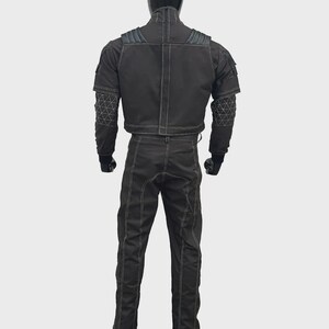 Puede incluir: Un conjunto de chaqueta y pantal&oacute;n de estilo t&aacute;ctico en color negro con costuras blancas en contraste. La chaqueta incluye hombreras, cuello alto y patrones geom&eacute;tricos de l&iacute;neas blancas en las mangas. El pantal&oacute;n tiene un corte recto.