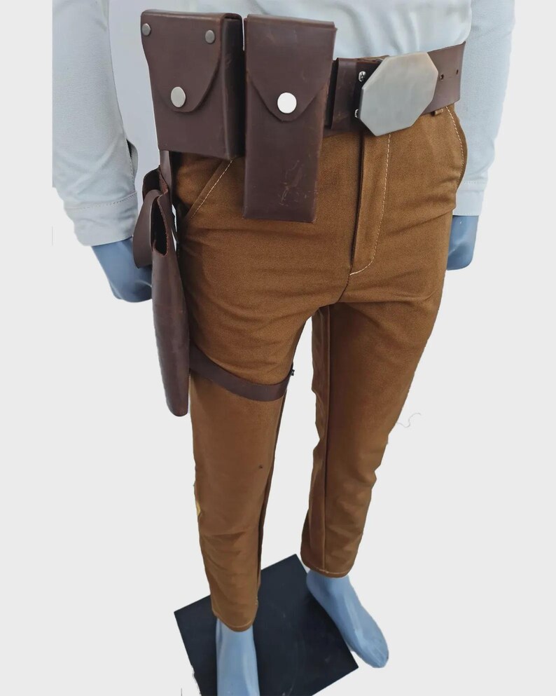 May include: Brown trousers paired with a dark brown leather utility belt featuring two rectangular pouches, a silver-toned hexagonal buckle, and a matching brown leather holster attached to the belt and thigh with a strap.