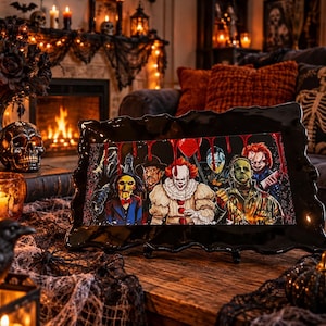 May include: A rectangular black frame with a wavy, irregular edge containing a colourful illustration of various horror movie characters, including a clown, a doll, and masked figures, with red blood-like drips running down the top of the image.