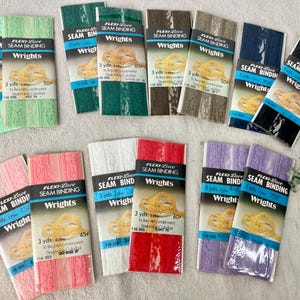 May include: Assortment of Flexi-Lace Seam Binding by Wrights in various colors, including green, pink, white, red, and purple. Each package contains 3 yards of binding. The packages have a blue and black label.