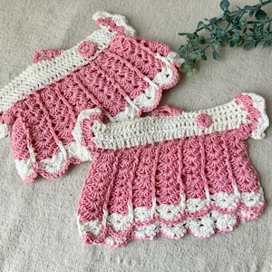 May include: Two handmade crochet pieces in pink and white. The pieces have a scalloped edge and a floral design. One piece is a top with a collar and the other is a matching piece. The items are displayed on a neutral surface.