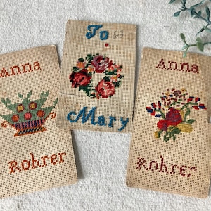 May include: Three vintage needlepoint pieces with floral and geometric designs. Two pieces read "Anna" and "Rohrer", one reads "To Mary". The needlepoint features red, blue, green, and yellow thread on a beige background.