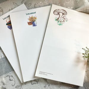 May include: Three sheets of white stationery paper. The left sheet features a basket illustration with the text Longaberger. The middle sheet shows a basket and floral arrangement with the text Longaberger. The right sheet displays a mushroom illustration.