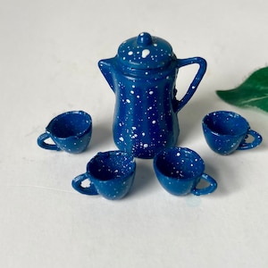 May include: A miniature blue enamelware coffee pot with a matching set of four small cups. The set is speckled with white paint, giving it a rustic, vintage appearance. Perfect for a dollhouse or miniature collection.