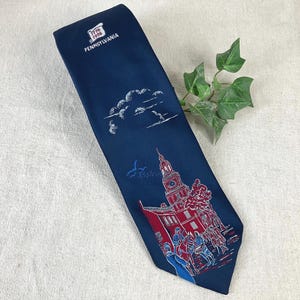 May include: A navy blue tie featuring a detailed illustration of Independence Hall in red and white, with figures and the text "Pennsylvania". The tie also includes white clouds and the text "1776-1976".